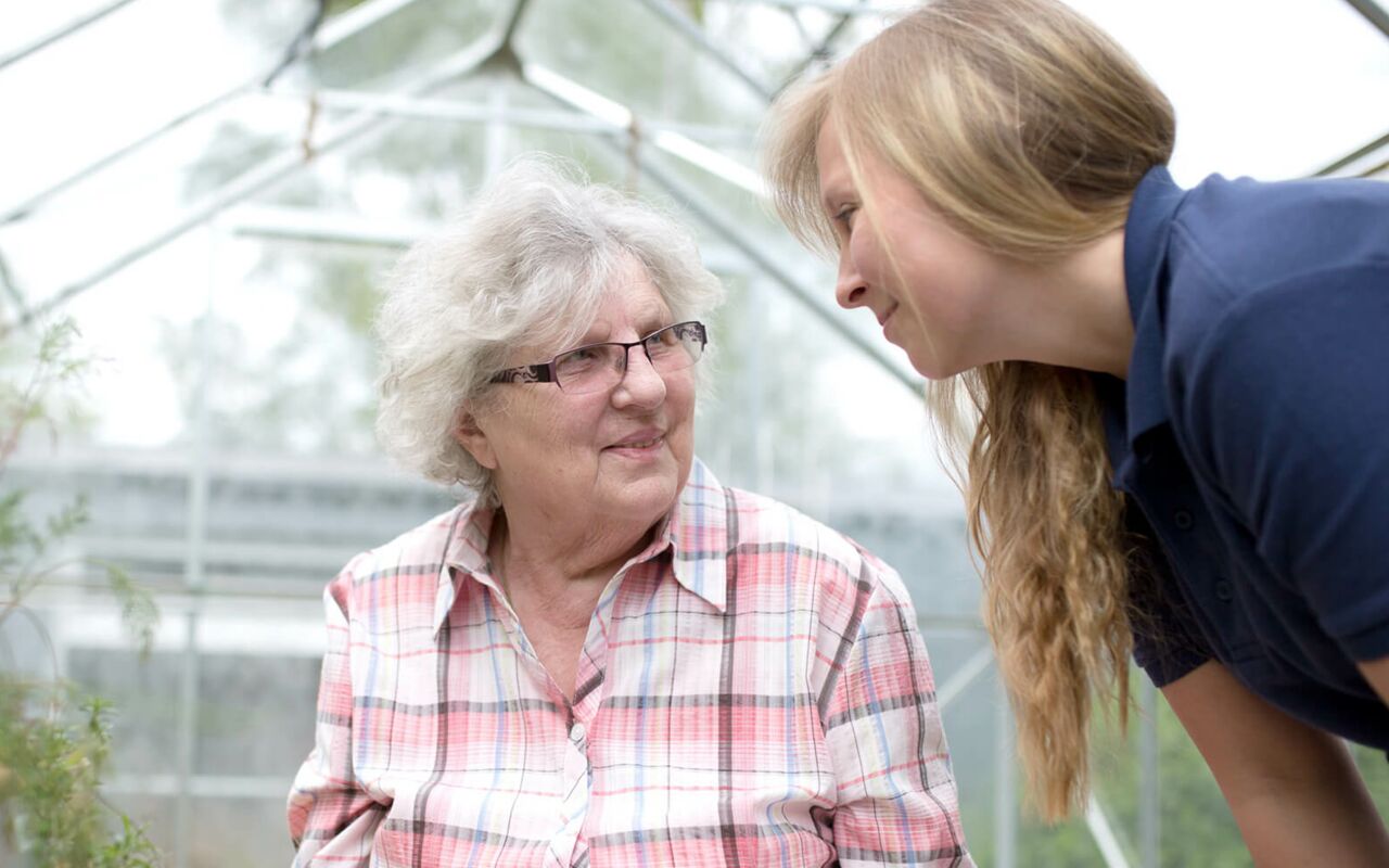 Hüttenhospital - Eine Seniorin schaut lächelnd eine Pflegerin an